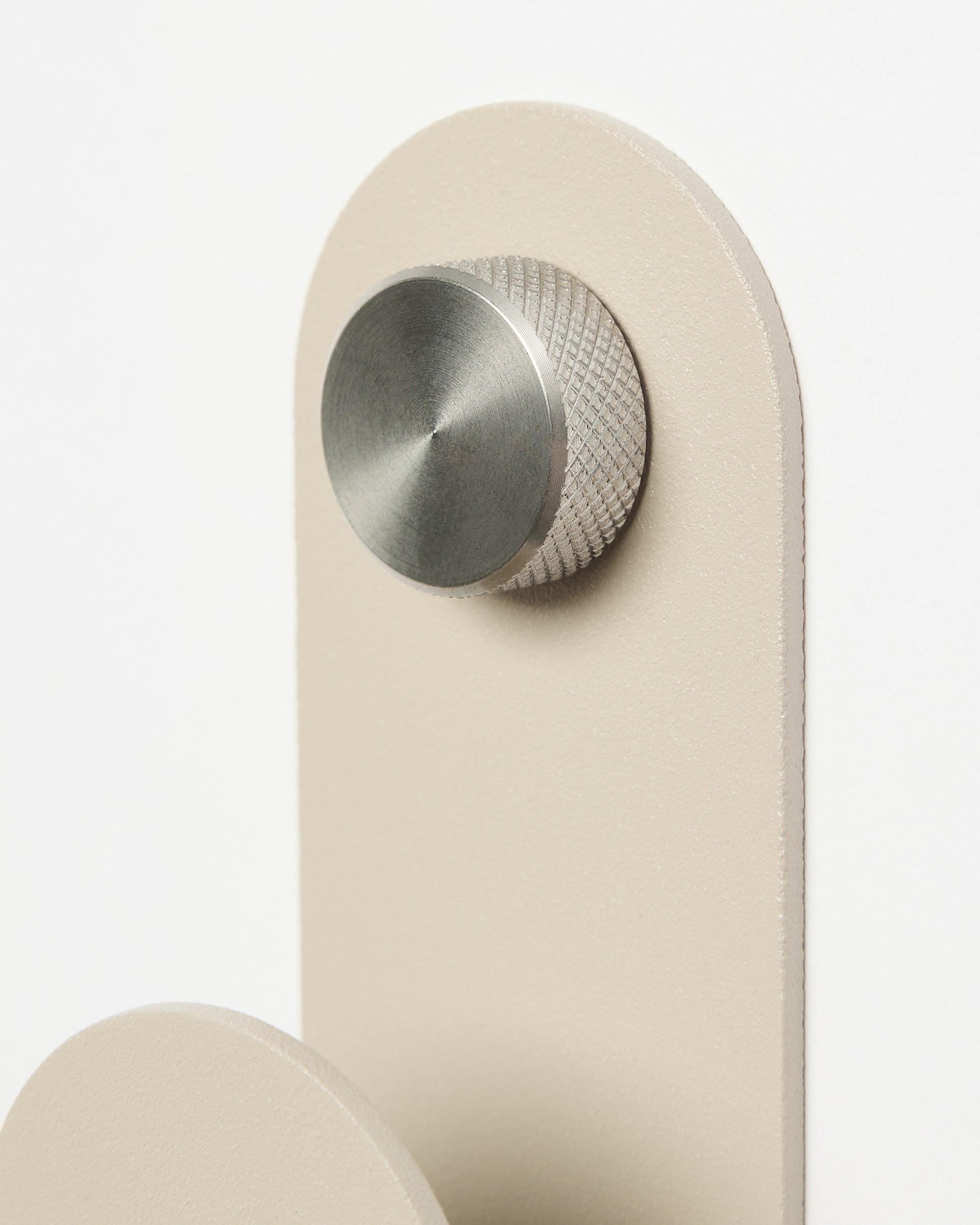 A round, metallic knob installed on a beige, vertically-oriented rectangular Akupanel accessory plate, set against a white background.